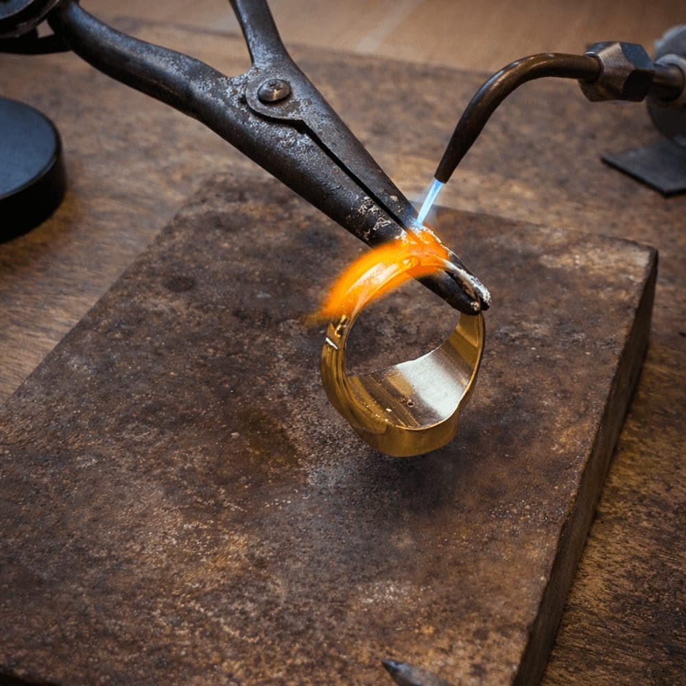 Gullsmed lodder en sprukket gullring med presisjonsflamme på verkstedet